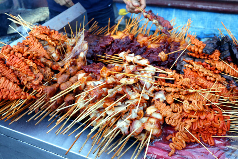 Filipino street food stall at night serving isaw, fish balls, and kwek-kwek.